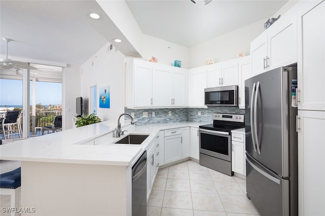 kitchen with kitchen peninsula, light stone counters, stainless steel appliances, sink, and white cabinetry