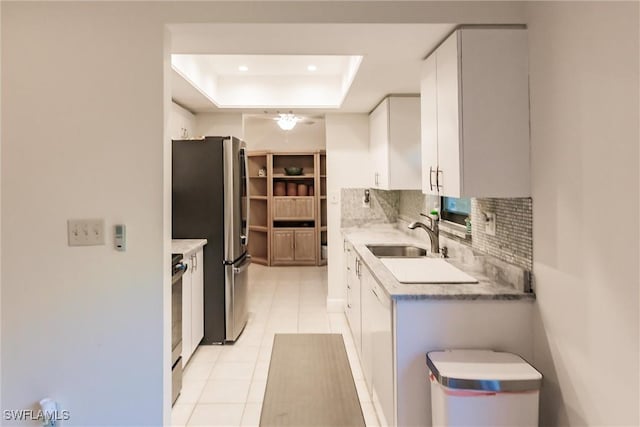 kitchen with stove, sink, a tray ceiling, stainless steel refrigerator, and white cabinets