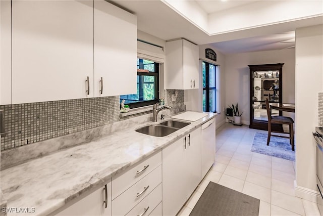 kitchen with dishwasher, sink, light tile patterned floors, light stone countertops, and white cabinets