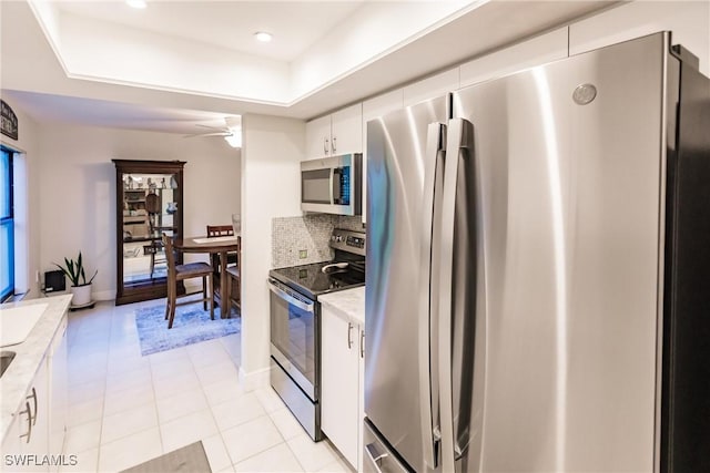 kitchen featuring white cabinetry, appliances with stainless steel finishes, backsplash, a tray ceiling, and light tile patterned flooring