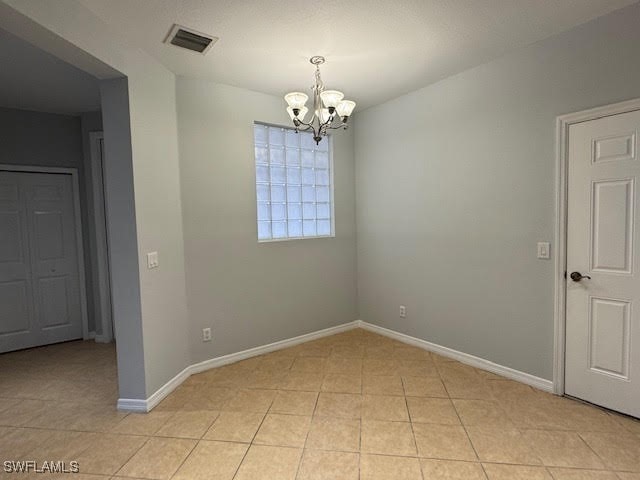 empty room featuring a notable chandelier and light tile patterned flooring