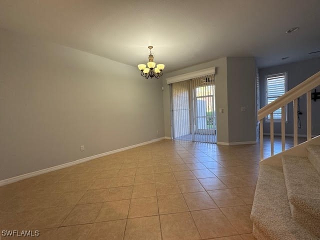 empty room with light tile patterned floors and a notable chandelier