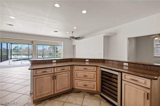 kitchen with ceiling fan, light brown cabinets, beverage cooler, dark stone countertops, and light tile patterned flooring