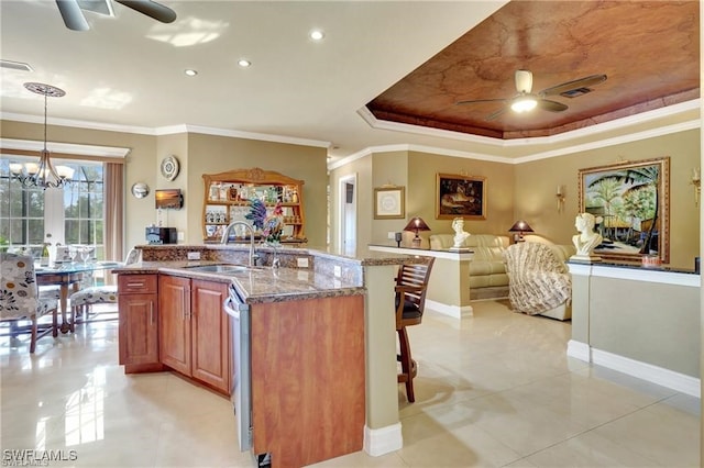 kitchen featuring sink, hanging light fixtures, a tray ceiling, stone counters, and ceiling fan with notable chandelier