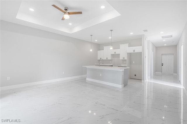 kitchen with pendant lighting, a raised ceiling, an island with sink, and white cabinets