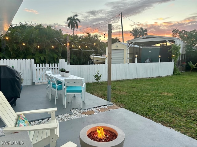 patio terrace at dusk featuring area for grilling, a yard, and a fire pit