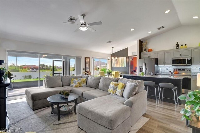 living room featuring vaulted ceiling, ceiling fan with notable chandelier, and light hardwood / wood-style flooring