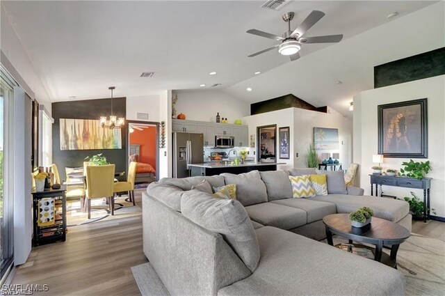 living room featuring vaulted ceiling, ceiling fan with notable chandelier, and light wood-type flooring