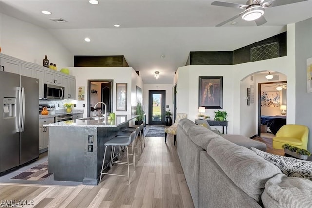 kitchen featuring stainless steel appliances, an island with sink, sink, ceiling fan, and a breakfast bar