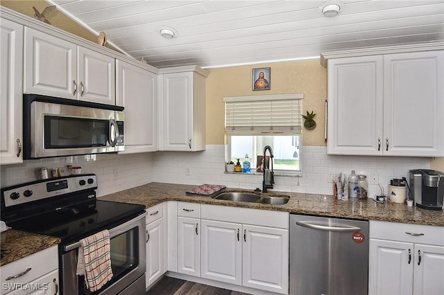 kitchen featuring stainless steel appliances, backsplash, white cabinets, a sink, and dark stone countertops