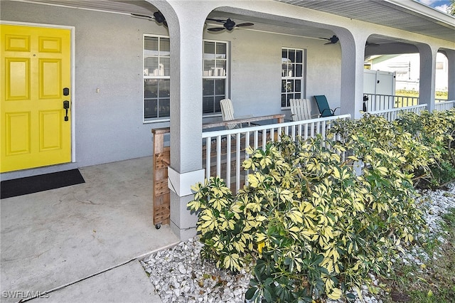 entrance to property featuring a porch, ceiling fan, and stucco siding