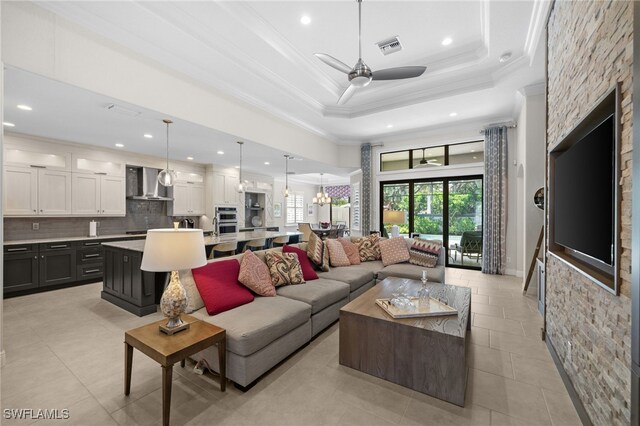 living room with crown molding, a tray ceiling, and ceiling fan with notable chandelier