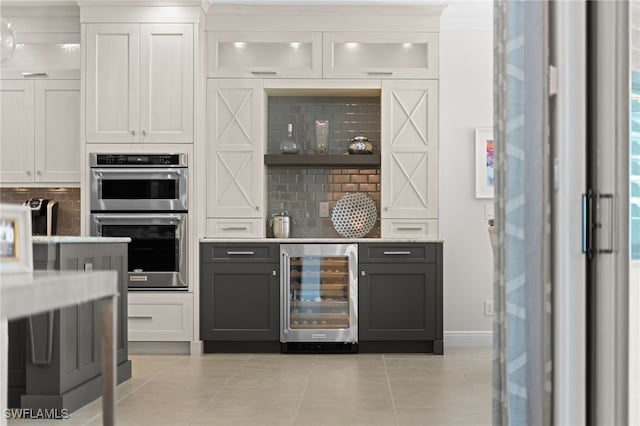 bar featuring tasteful backsplash, light tile patterned floors, double oven, beverage cooler, and white cabinets