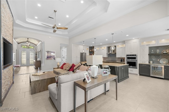 tiled living room featuring ornamental molding, a tray ceiling, wine cooler, and french doors