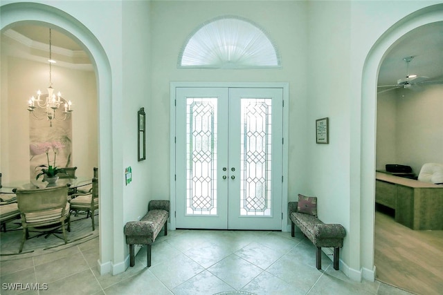 entryway featuring french doors, ceiling fan with notable chandelier, crown molding, and light tile patterned flooring