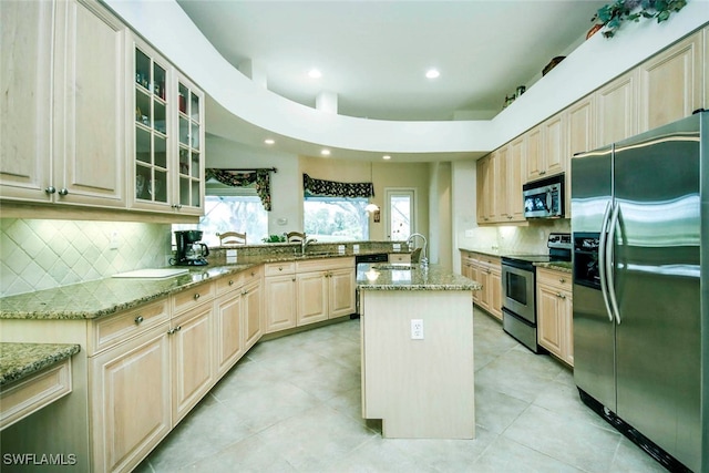 kitchen featuring decorative backsplash, a center island, stainless steel appliances, and light stone counters