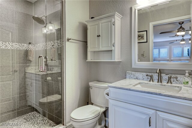 bathroom featuring vanity, a shower with shower door, toilet, and ceiling fan