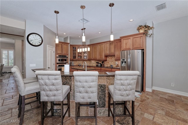 kitchen featuring decorative backsplash, an island with sink, appliances with stainless steel finishes, a breakfast bar, and pendant lighting