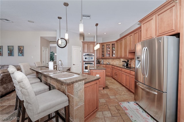 kitchen with backsplash, appliances with stainless steel finishes, a kitchen island with sink, pendant lighting, and sink