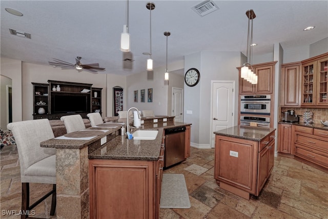 kitchen featuring sink, an island with sink, ceiling fan, stainless steel appliances, and decorative light fixtures