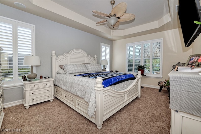 bedroom with ceiling fan, a tray ceiling, multiple windows, and light colored carpet