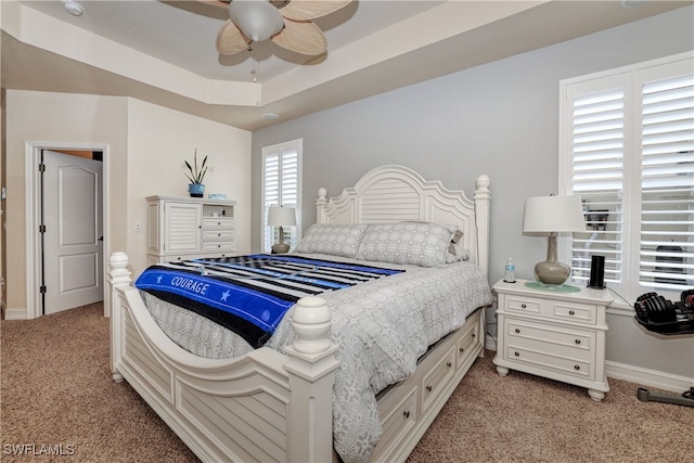 bedroom with light carpet, a tray ceiling, and ceiling fan