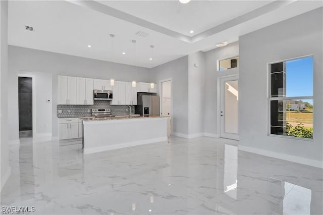 kitchen with hanging light fixtures, a high ceiling, a center island with sink, white cabinets, and appliances with stainless steel finishes