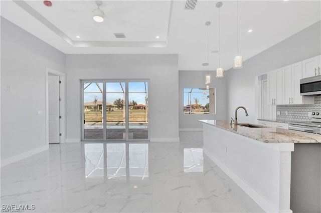 kitchen with sink, stainless steel appliances, hanging light fixtures, light stone counters, and white cabinets