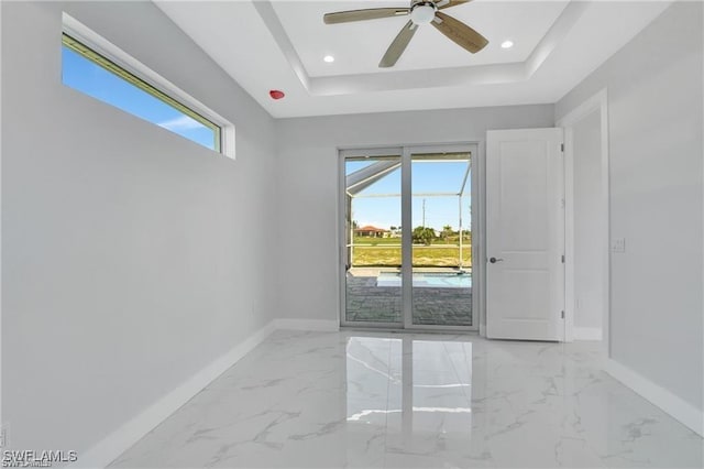 unfurnished room featuring a raised ceiling, a wealth of natural light, and ceiling fan