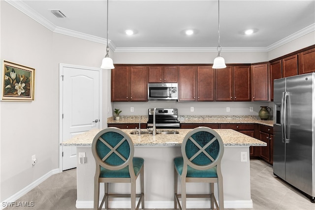 kitchen featuring appliances with stainless steel finishes, hanging light fixtures, an island with sink, and light stone countertops