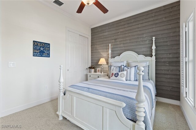 bedroom with crown molding, wooden walls, ceiling fan, light colored carpet, and a closet