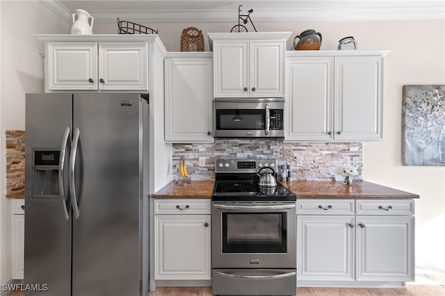 kitchen with appliances with stainless steel finishes, tasteful backsplash, ornamental molding, dark stone countertops, and white cabinetry