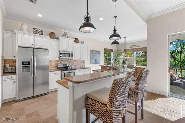 kitchen featuring a kitchen bar, white cabinetry, hanging light fixtures, and appliances with stainless steel finishes