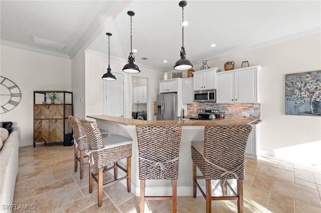 kitchen featuring white cabinets, light countertops, appliances with stainless steel finishes, backsplash, and a kitchen bar