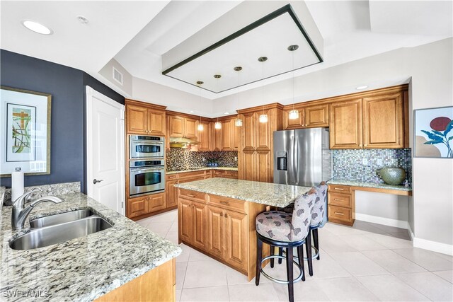 kitchen featuring light stone counters, stainless steel appliances, pendant lighting, decorative backsplash, and sink