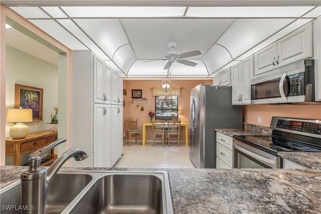 kitchen featuring light tile patterned floors, stainless steel appliances, a sink, a ceiling fan, and dark stone countertops