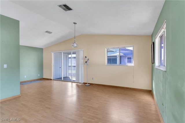 spare room with a textured ceiling, light wood-type flooring, and vaulted ceiling