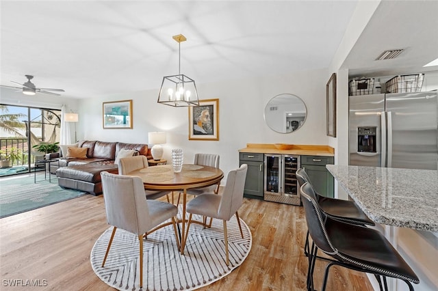 dining space featuring light hardwood / wood-style flooring, wine cooler, and ceiling fan with notable chandelier