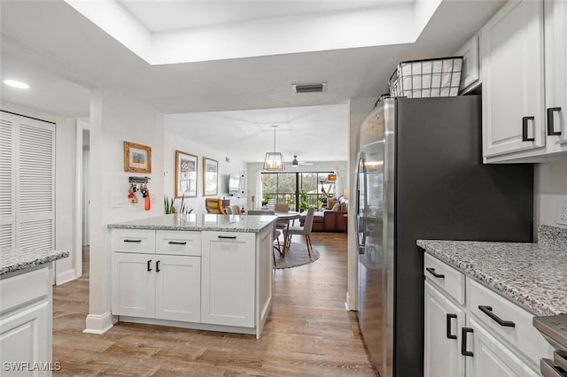 kitchen with light wood-type flooring, stainless steel fridge, white cabinetry, pendant lighting, and light stone counters