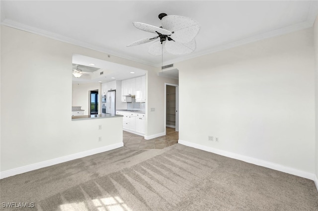 unfurnished living room with ceiling fan, a raised ceiling, ornamental molding, and light colored carpet