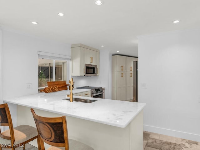 kitchen with light stone countertops, a sink, stainless steel appliances, a breakfast bar, and a peninsula