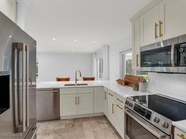 kitchen featuring stainless steel appliances, stone finish floor, light countertops, a sink, and a peninsula