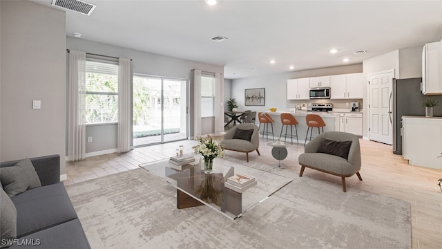 living room with baseboards, light wood-style flooring, visible vents, and recessed lighting