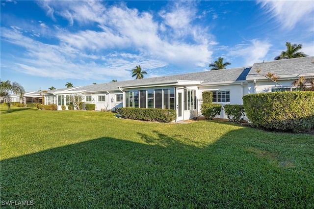 rear view of house featuring a yard, a sunroom, and stucco siding