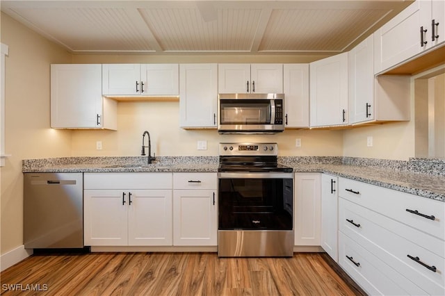 kitchen featuring light wood-type flooring, white cabinets, light stone countertops, stainless steel appliances, and a sink