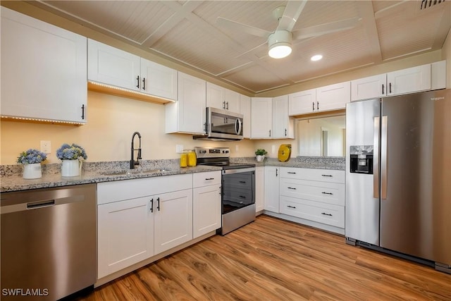 kitchen with stainless steel appliances, white cabinetry, sink, and light hardwood / wood-style flooring