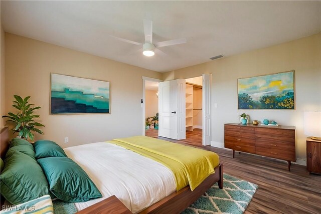 bedroom featuring baseboards, a spacious closet, a ceiling fan, visible vents, and wood finished floors