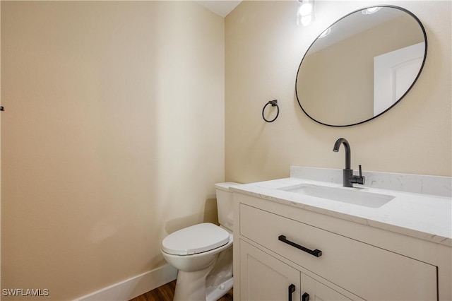 half bath featuring vanity, baseboards, toilet, and wood finished floors