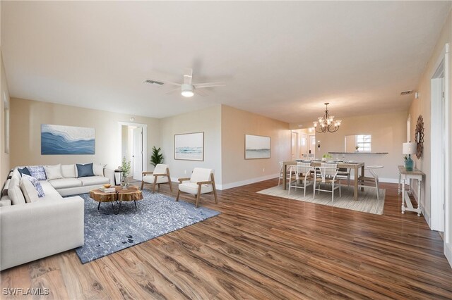 living area featuring visible vents, baseboards, wood finished floors, and ceiling fan with notable chandelier