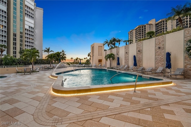 pool at dusk with pool water feature and a patio area